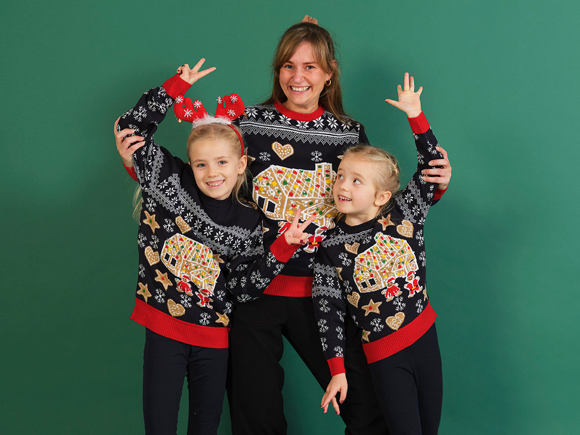 En dame og to børn poserer i blå julesweatre med kagehuse og kagepersoner på.